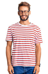 Handsome blond man with beard wearing casual clothes and glasses winking looking at the camera with...
