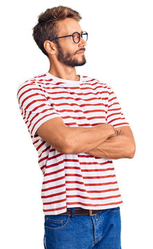 Handsome blond man with beard wearing casual clothes and glasses looking to the side with arms crossed convinced and confident