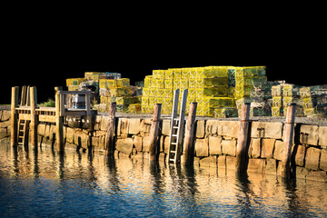 Fototapeta premium Brilliant yellow lobster traps on wharf at sunset with jet black background