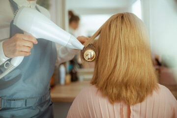 Woman hairdresser in beauty salon blowout hair with hair dryer