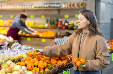 Young woman in casual clothes buys tangerines in greengrocer's shop