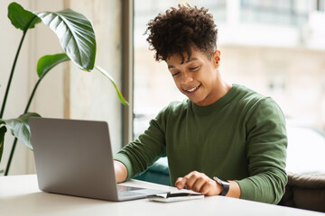 Happy millennial black man using gadgets at cafe