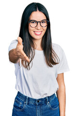 Young hispanic woman wearing casual clothes and glasses smiling friendly offering handshake as greeting and welcoming. successful business.