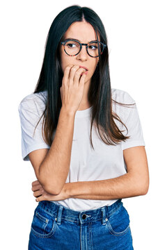 Young hispanic woman wearing casual clothes and glasses looking stressed and nervous with hands on mouth biting nails. anxiety problem.