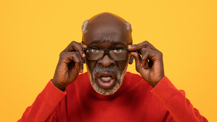 Surprised senior Black man adjusting his glasses with a puzzled expression