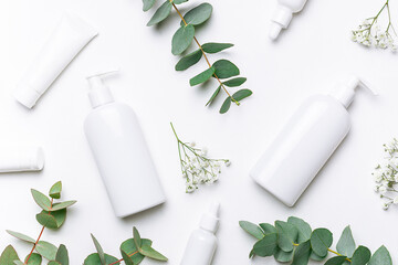 Set of organic eco skin care products in white unbranded containers , beautiful flowers and eucalyptus leaves on white background top view. Cosmetic branding concept. - obrazy, fototapety, plakaty