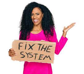 Middle age african american woman holding fix the system banner cardboard celebrating victory with happy smile and winner expression with raised hands