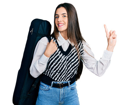 Young brunette teenager wearing guitar case smiling with an idea or question pointing finger with happy face, number one
