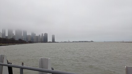 Chicago skyline and the Navy Pier disappearing into fog, with a choppy Lake Michigan in the foreground. Taken in downtown Chicago, specifically of Navy Pier, on a rainy, snowy day.