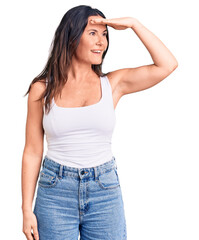 Young beautiful brunette woman wearing casual sleeveless t-shirt very happy and smiling looking far away with hand over head. searching concept.