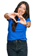 Beautiful brunette young woman wearing casual clothes smiling in love doing heart symbol shape with...