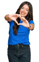 Fototapeten Beautiful brunette young woman wearing casual clothes smiling in love doing heart symbol shape with hands. romantic concept. © Krakenimages.com