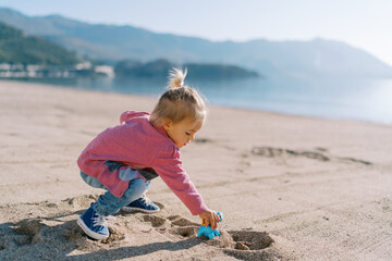 Little girl plays on the sand on the beach with a toy plastic dinosaur