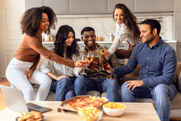 Diverse group of students clinking with beer on sofa indoors