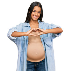 Beautiful hispanic woman expecting a baby showing pregnant belly smiling in love showing heart symbol and shape with hands. romantic concept.