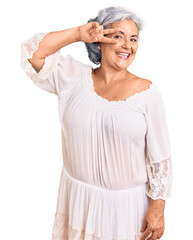 Senior woman with gray hair wearing bohemian style doing peace symbol with fingers over face, smiling cheerful showing victory