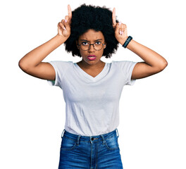 Young african american woman wearing casual white t shirt doing funny gesture with finger over head as bull horns