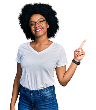 Young african american woman wearing casual white t shirt with a big smile on face, pointing with hand finger to the side looking at the camera.