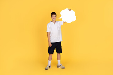 A cheerful young boy stands confidently, holding a large white speech bubble sign