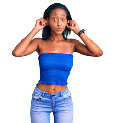 Young african american woman wearing casual summer clothes smiling pulling ears with fingers, funny...