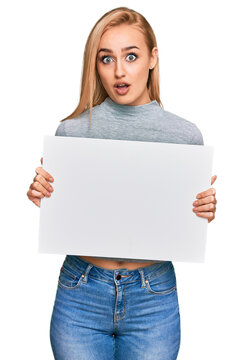 Beautiful caucasian woman holding blank empty banner scared and amazed with open mouth for surprise, disbelief face