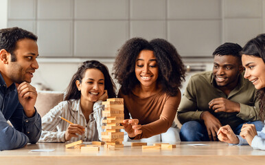 Young diverse friends engaged in board game building tower indoors