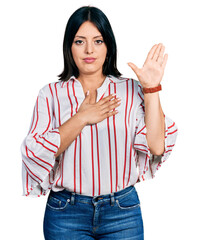 Young hispanic girl wearing casual clothes swearing with hand on chest and open palm, making a...