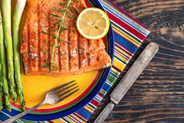 Baked salmon with asparagus on a yellow plate on a dark wooden table.