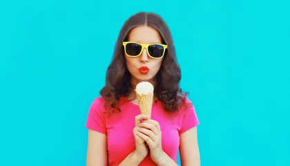 Foto op Plexiglas Summer portrait of happy young woman eating ice cream wearing sunglasses on blue background © rohappy