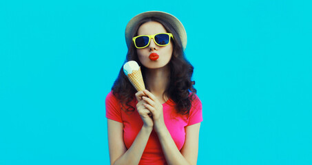 Summer portrait of happy young woman eating ice cream wearing sunglasses on blue background