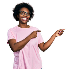 African american woman with afro hair wearing casual clothes and glasses smiling and looking at the camera pointing with two hands and fingers to the side.