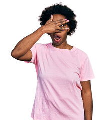 Fototapeta na wymiar African american woman with afro hair wearing casual clothes and glasses peeking in shock covering face and eyes with hand, looking through fingers with embarrassed expression.