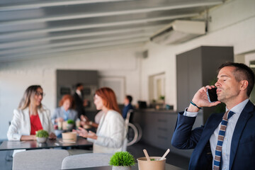 Worker resolving incidents through the mobile phone in the rest area with his colleagues talking - Concept: Business