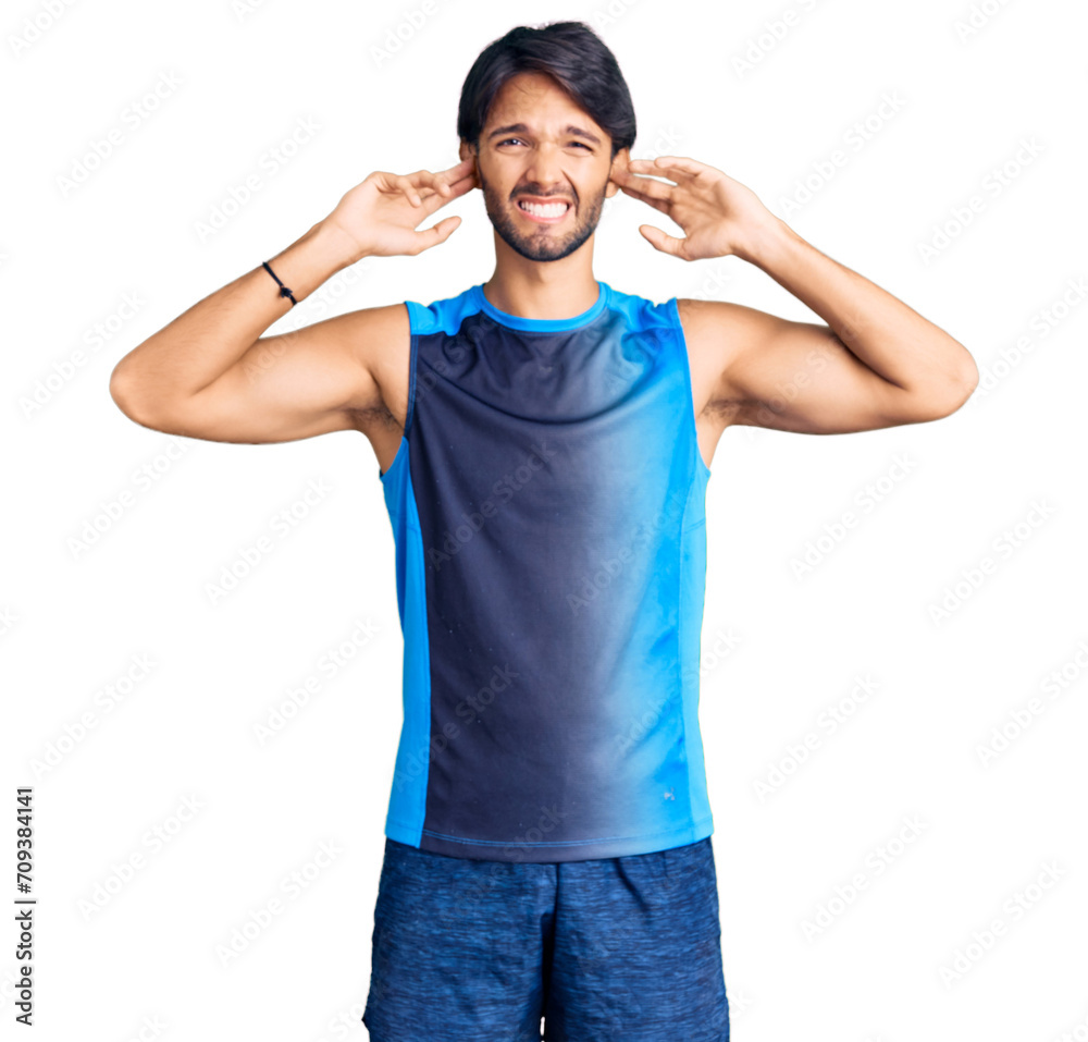 Poster handsome hispanic man wearing sportswear covering ears with fingers with annoyed expression for the 