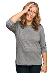 Fototapeta premium Middle age blonde woman wearing casual clothes smiling happy doing ok sign with hand on eye looking through fingers