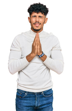 Young arab man wearing casual winter sweater begging and praying with hands together with hope expression on face very emotional and worried. begging.