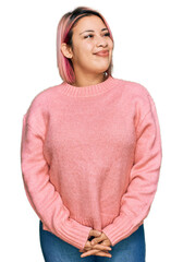 Hispanic woman with pink hair wearing casual winter sweater smiling looking to the side and staring...