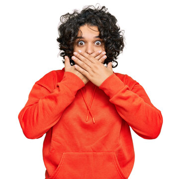 Young hispanic woman with curly hair wearing casual sweatshirt shocked covering mouth with hands for mistake. secret concept.