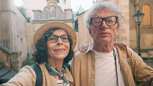 Old Caucasian male talking to woman while she trying to make photo of them together. Woman pointing at camera. Trying to make man focus and smile to make lovely picture. Concept of love.