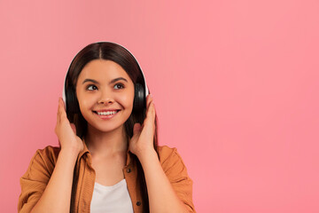 Smiling teenage girl wearing wireless headphones listening music, hands touching the earcups