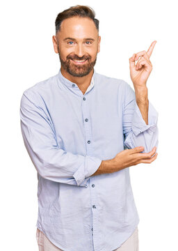 Handsome middle age man wearing business shirt with a big smile on face, pointing with hand and finger to the side looking at the camera.