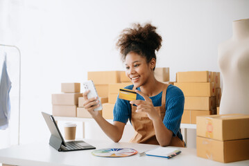 Young woman holding a smartphone, tablet showing payment success and credit card with yellow parcel box as online shopping concept