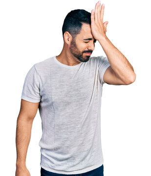 Young hispanic man with beard wearing casual grey t shirt surprised with hand on head for mistake, remember error. forgot, bad memory concept.