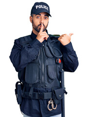 Young hispanic man wearing police uniform asking to be quiet with finger on lips pointing with hand...