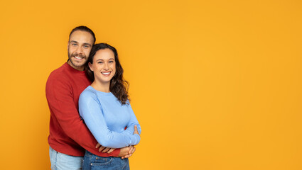 Loving millennial couple embracing on orange studio background - obrazy, fototapety, plakaty