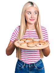 Beautiful blonde woman eating pastries smiling looking to the side and staring away thinking.