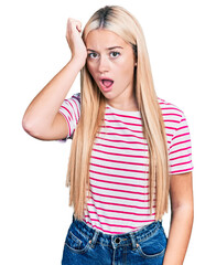 Beautiful blonde woman wearing casual striped t shirt surprised with hand on head for mistake,...