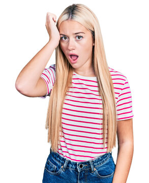 Beautiful blonde woman wearing casual striped t shirt surprised with hand on head for mistake, remember error. forgot, bad memory concept.