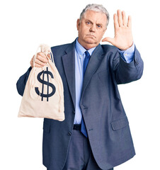 Senior grey-haired man wearing business suit holding money bag with dollar symbol with open hand...