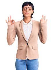 Young brunette woman with short hair wearing business jacket and glasses relax and smiling with eyes closed doing meditation gesture with fingers. yoga concept.